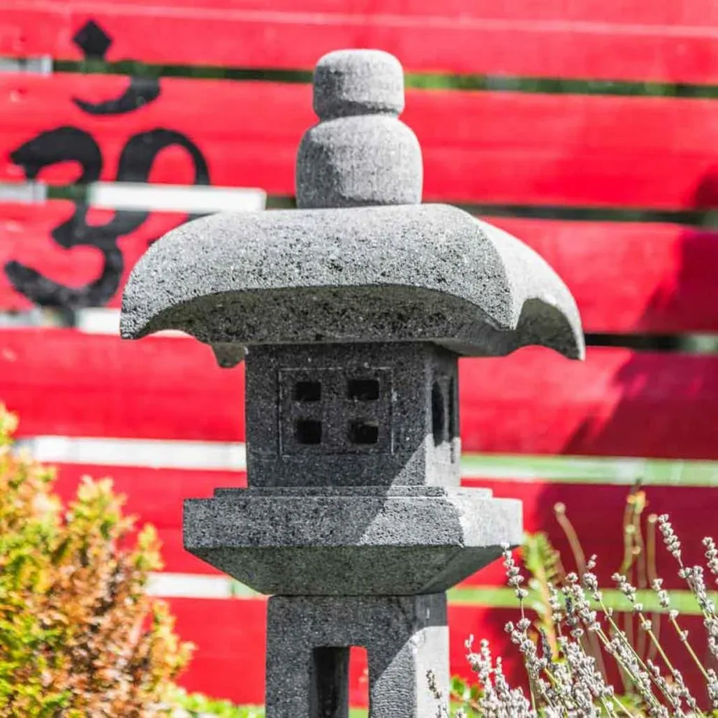 Lanterne japonaise en pierre de lave devant une clôture rouge décorée du symbole Om