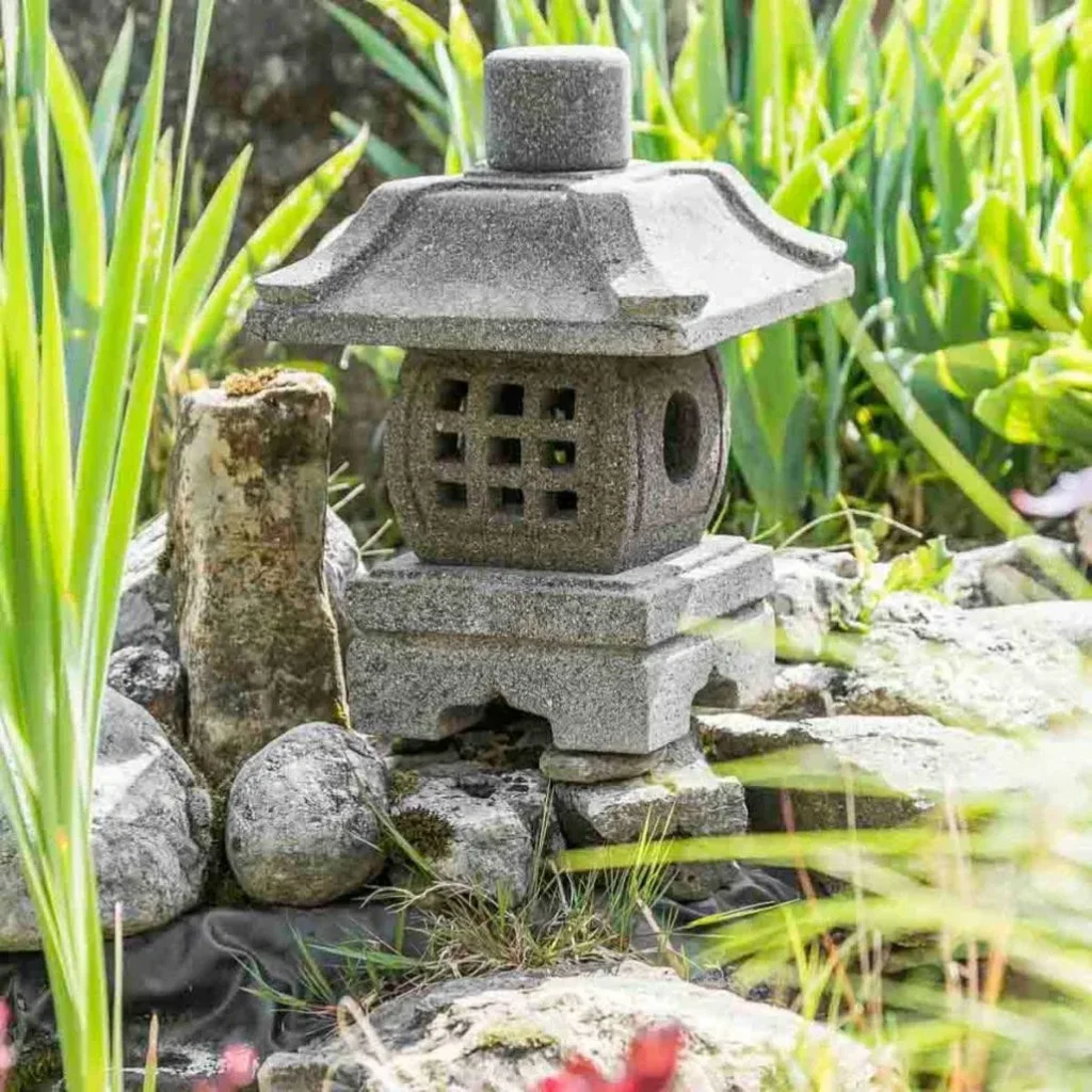 Petite lanterne japonaise en pierre dans un jardin zen entourée de roches et de végétation