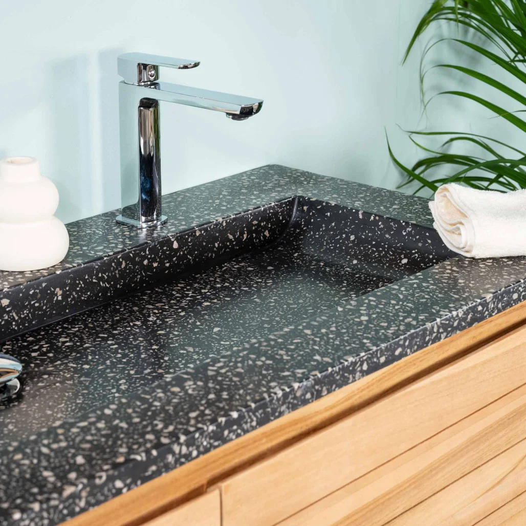 Plan vasque en terrazzo noir avec robinet chromé, intégré à un meuble de salle de bain en bois