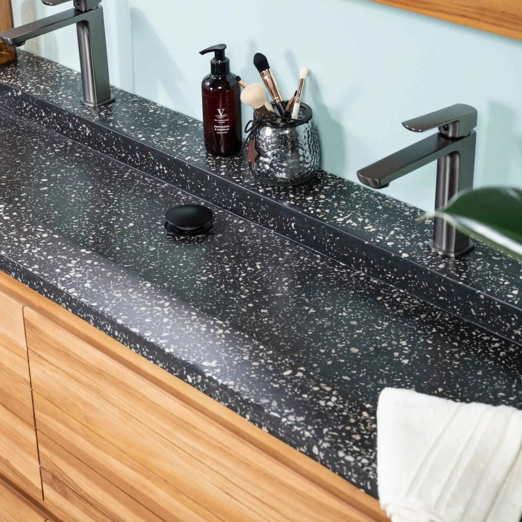 Plan vasque en terrazzo noir avec double robinet, installé sur un meuble de salle de bain en bois